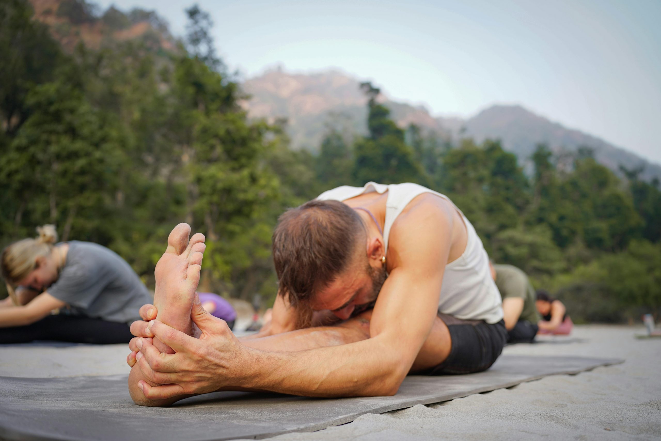 yoga practitioners doing seated leg stretches in a forested area
