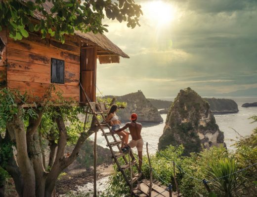 couple standing on a treehouse ladder overlooking a beach in Bali