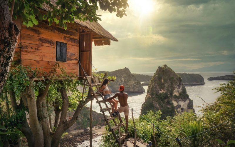 couple standing on a treehouse ladder overlooking a beach in Bali