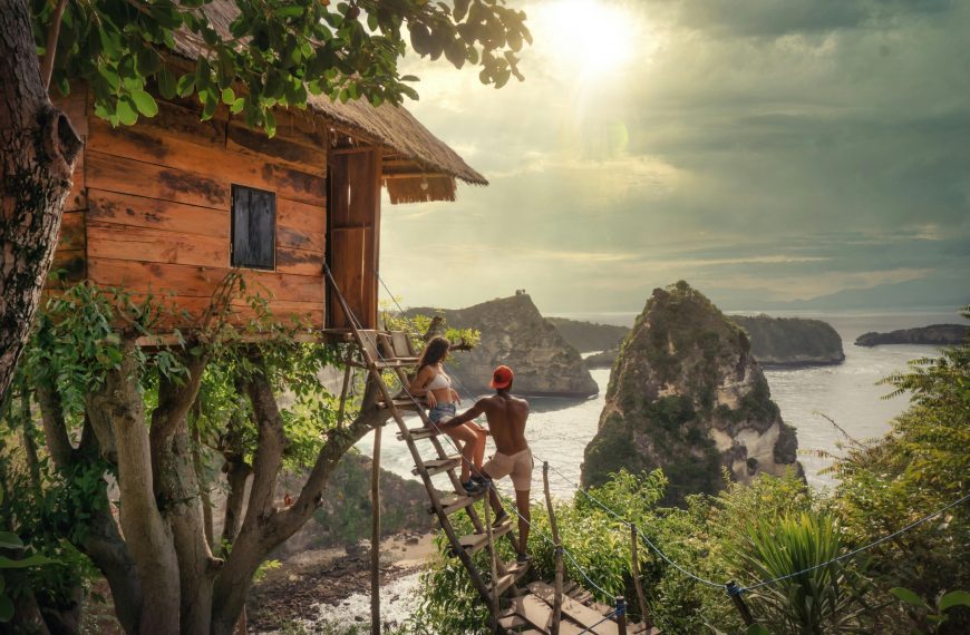 couple standing on a treehouse ladder overlooking a beach in Bali
