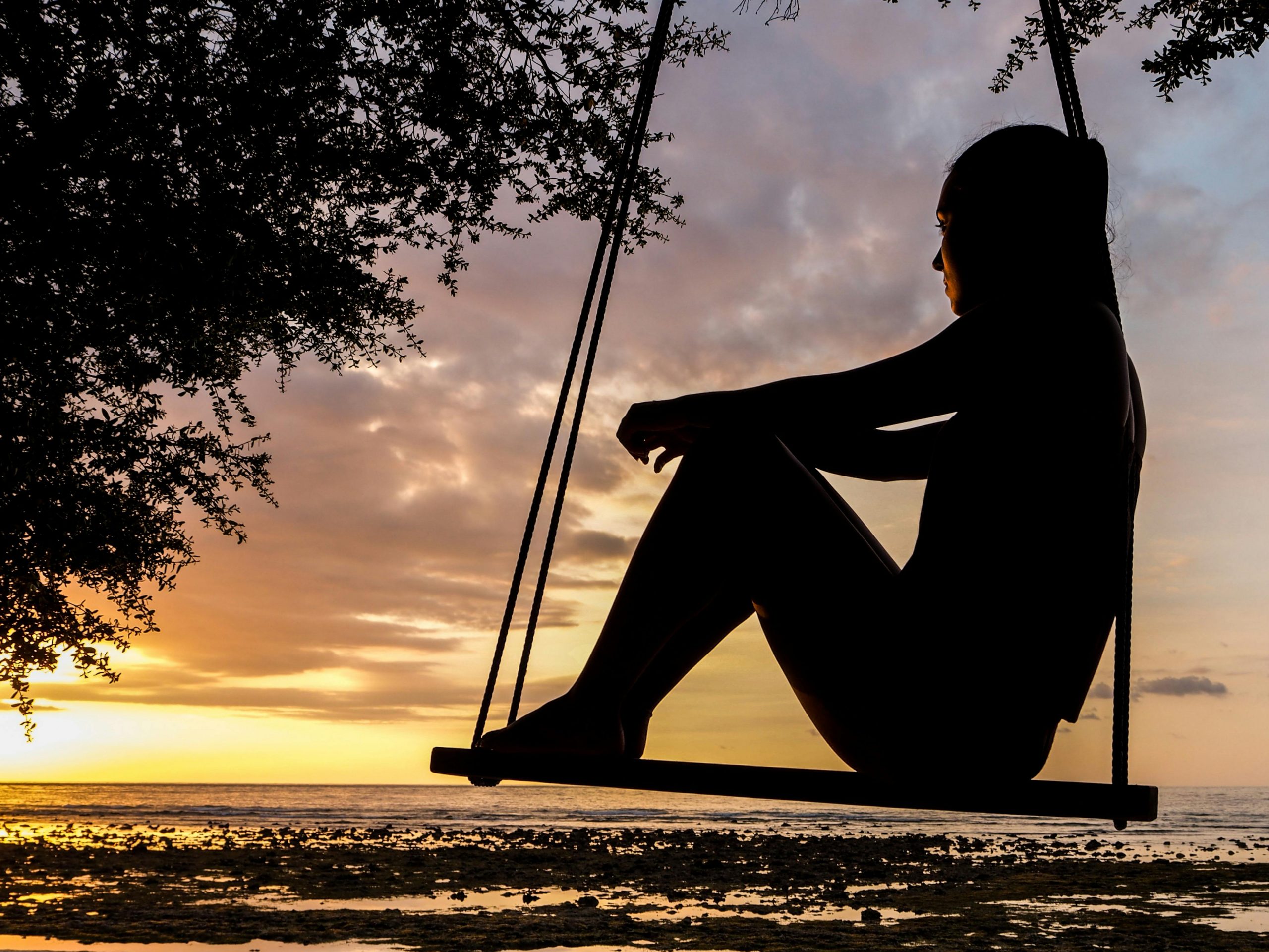 silhouette of a woman sitting on a swing viewing the sunset on the beach